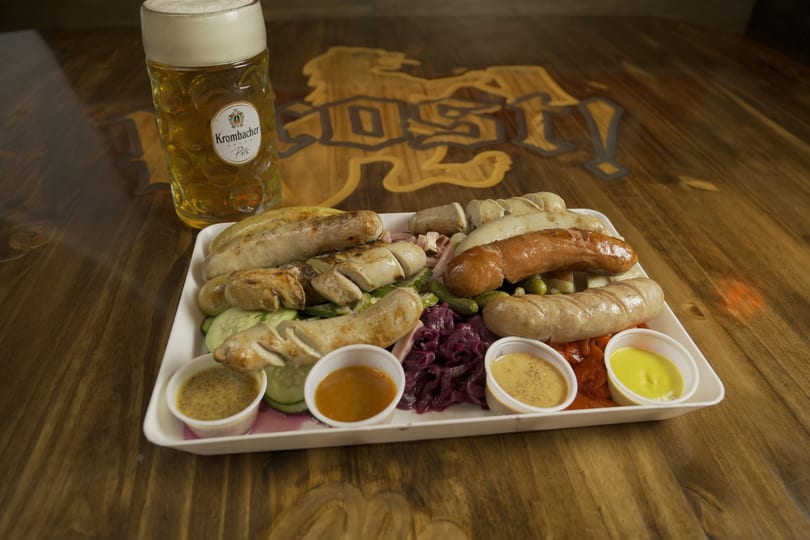 A platter of various sausages, red cabbage, pickles, and sauces, with a beer stein.