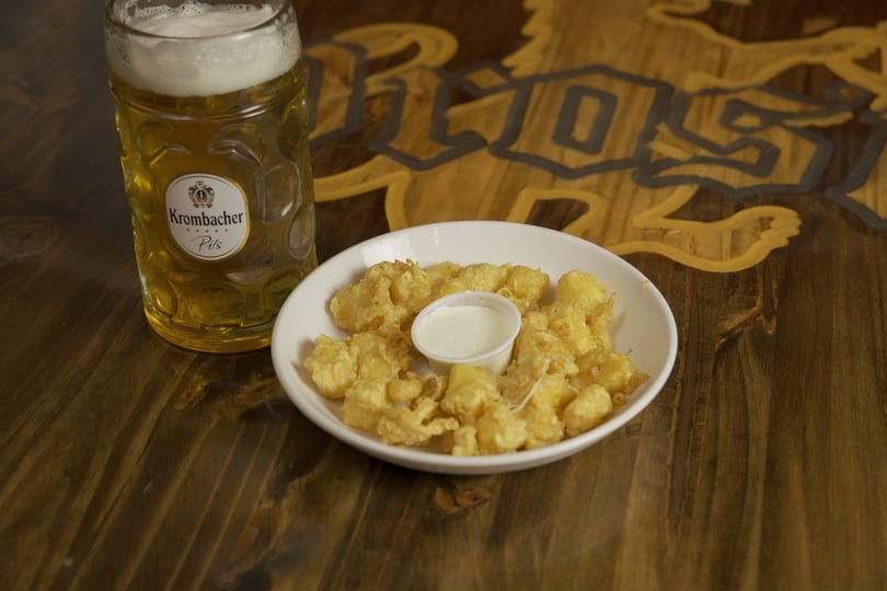 A glass of Krombacher Pils beer and a plate of fried cheese curds with ranch dressing.